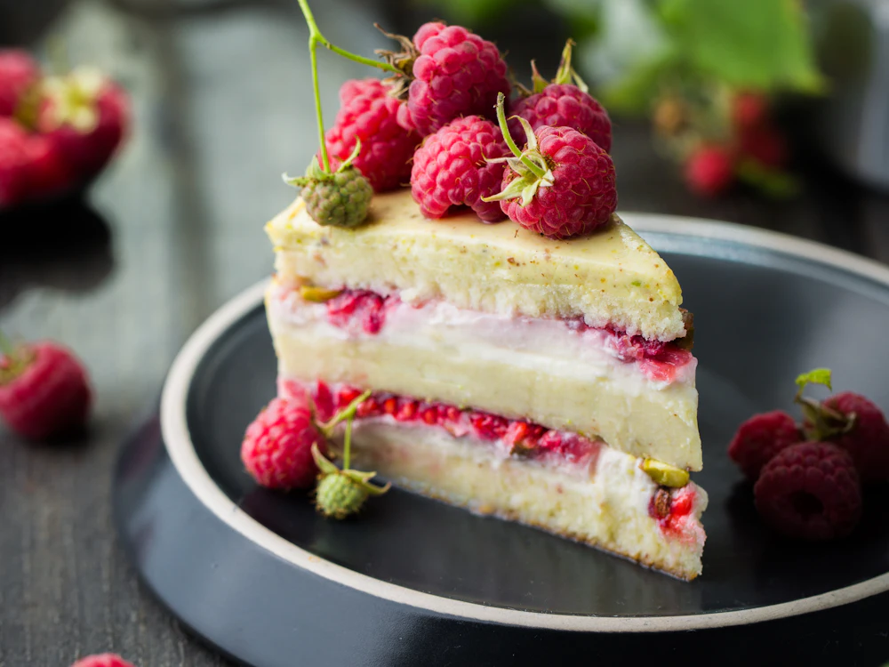 Raspberry layer cake slice with fresh berries on a dark plate